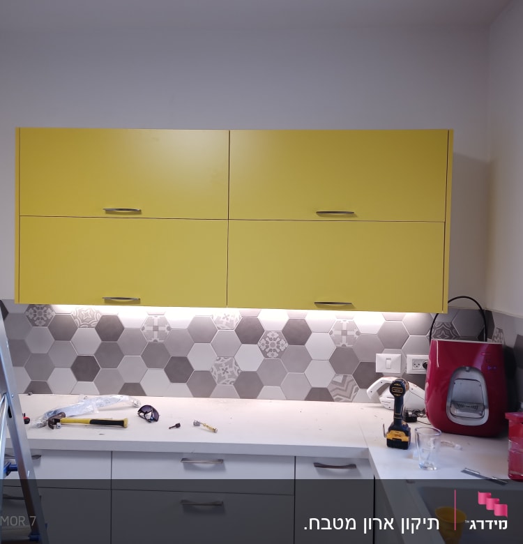סולם, כלים על השיש, מקדחה, ארונות מטבח צהובים